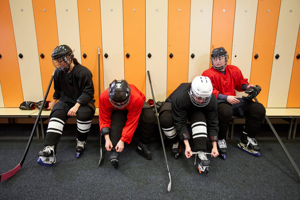 Высокоугольный вид на женскую хоккейную команду, надевающую экипировку в раздевалке при подготовке к матчу или тренировке, копирующее пространство
 - Фото, изображение