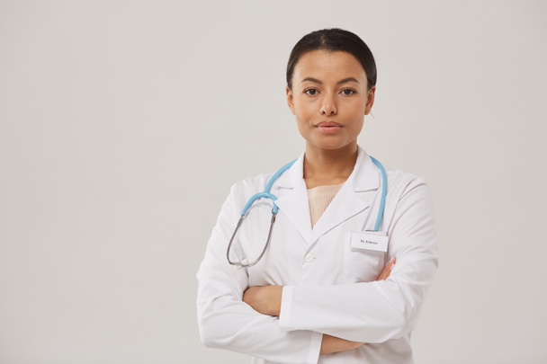 Cintura-se retrato de bela enfermeira afro-americana posando com confiança enquanto de pé com os braços cruzados contra fundo branco, espaço cópia
 - Foto, Imagem