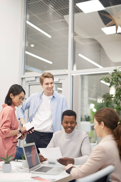 Multiethnische Gruppe junger Geschäftsleute diskutiert Arbeitsprojekt und lächelt bei Treffen im Büro fröhlich - Foto, Bild