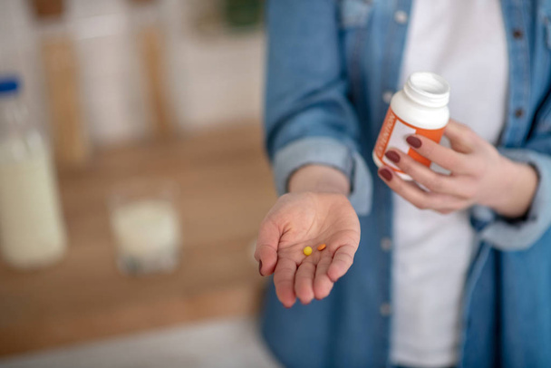Woman holding two pills and a container in hands - Foto, Imagem