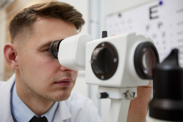 Zbliżenie portretu męskiego optometru z użyciem refraktometru podczas badania widzenia pacjenta nierozpoznawalnego - Zdjęcie, obraz