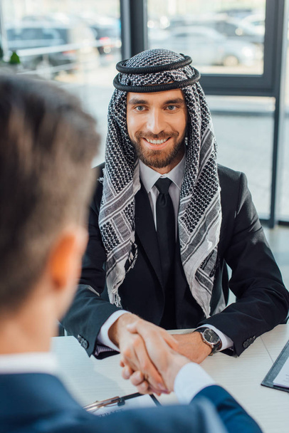 Lächelnder multiethnischer Geschäftsmann beim Händeschütteln mit Partner bei einem Treffen - Foto, Bild
