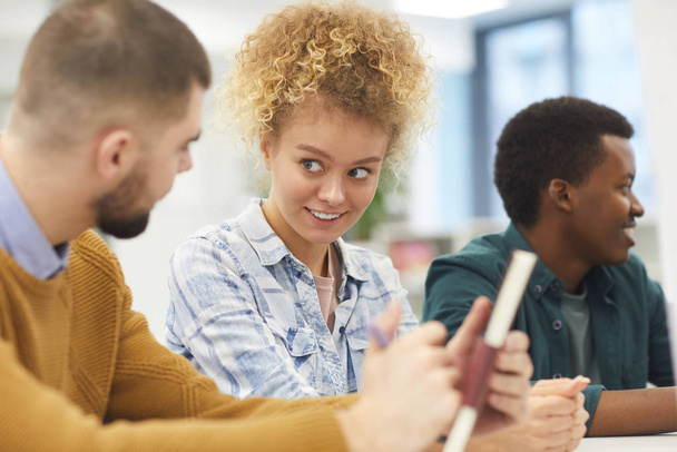 Grupo multiétnico de estudiantes sentados en el escritorio en clase, se centran en la alegre joven mujer sonriendo a su amigo
 - Foto, Imagen