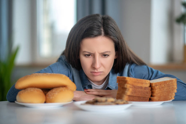 Woman looking at the plates with buns and bread - Фото, зображення