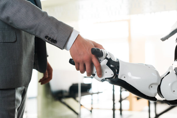 przycięty widok biznesmena i robota ściskającego dłonie w biurze - Zdjęcie, obraz