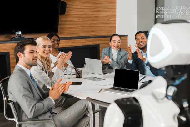 Selektiver Fokus multikultureller Geschäftsleute, die applaudieren, während sie Roboter im Büro betrachten - Foto, Bild