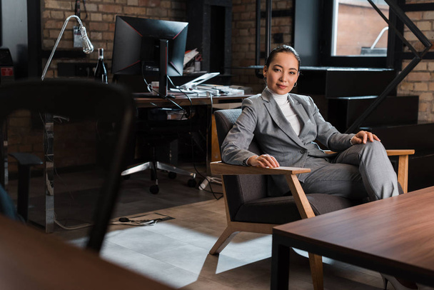 selektivní zaměření atraktivní asijské podnikatelky sedí v křesle v moderní kanceláři - Fotografie, Obrázek