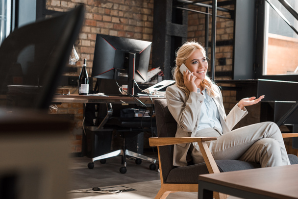 enfoque selectivo de la mujer de negocios sonriente sentada en sillón con el brazo abierto y hablando en el teléfono inteligente
 - Foto, Imagen
