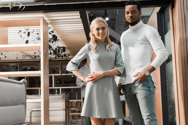 handsome african american businessman looking at camera with attractive colleague in office - Fotó, kép
