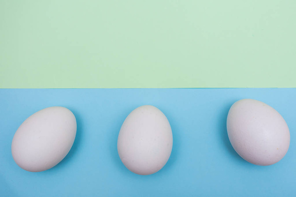 Drei Osterferienwohnung lag mit weißem Ei auf einem soliden hellgrünen über blauem Pastellhintergrund mit Kopierraum oben. - Foto, Bild