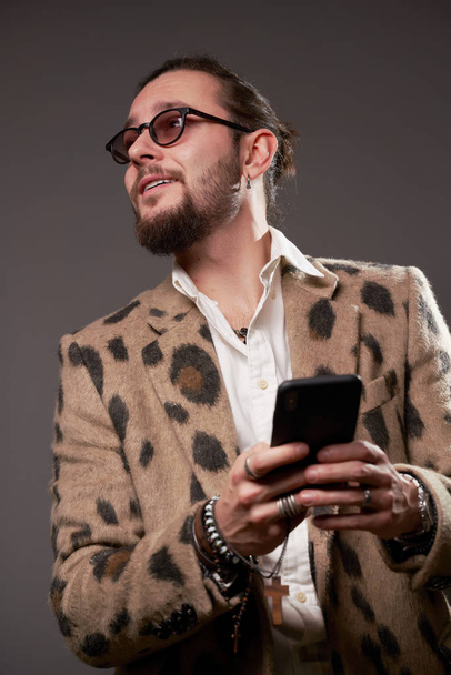 Man in sunglasses in jacket looking at side with phone in his hands on brown background - Photo, Image