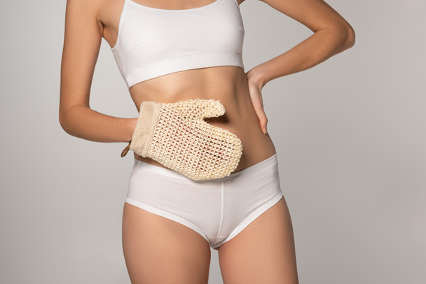 cropped view of slim girl with perfect skin holding scrub glove, isolated on grey - Foto, Imagem