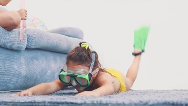 Little girl, wearing swimming suit, flippers and goggles imitating swimming, layinge on the carpet. Copy space. 4K. - Footage, Video