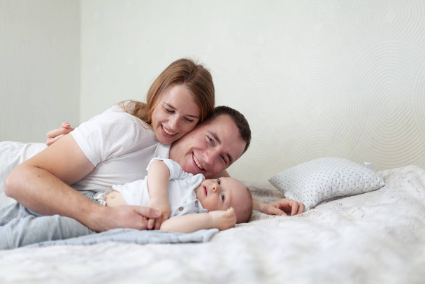 Πορτρέτο μιας ευτυχισμένης οικογένειας. Γονείς και μωρό αγκαλιάζονται και παίζουν στον καναπέ στο δωμάτιο - Φωτογραφία, εικόνα