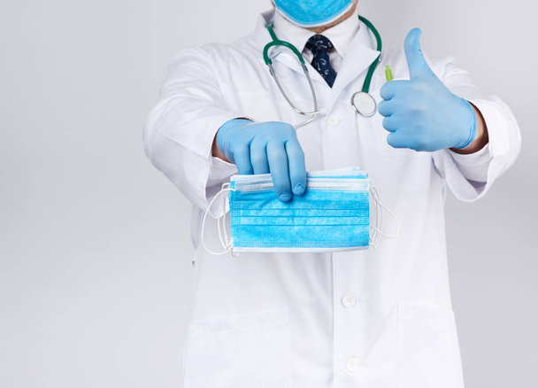 Врач в белом халате, голубые латексные стерильные перчатки держит текстиль
  - Фото, изображение