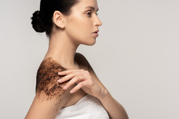 attractive young woman applying coffee scrub on shoulders, isolated on grey - Photo, Image