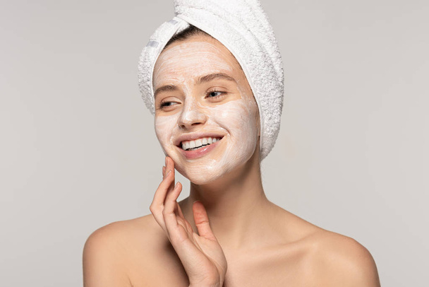 beautiful smiling girl with cosmetic mask on face and towel on head, isolated on grey  - Foto, Imagem