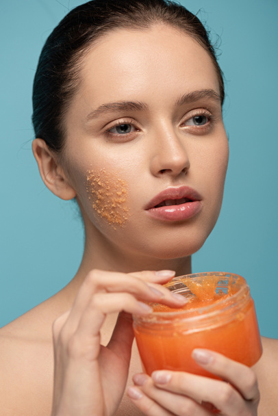 beautiful girl applying yellow sugar scrub from plastic container, isolated on blue - Fotó, kép