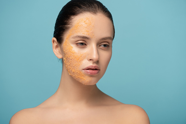 attractive girl applying yellow sugar exfoliant on face, isolated on blue - Foto, Imagem
