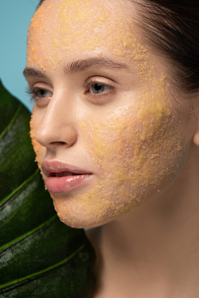 attractive girl with sugar scrub on face holding leaf, isolated on blue - Foto, Bild