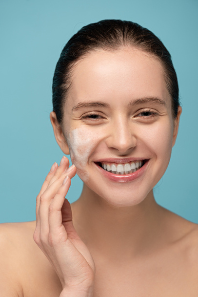 smiling girl applying cleansing foam on face, isolated on blue - Fotografie, Obrázek