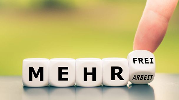 Hand turns dice and changes the German expression "mehr Arbeit"  - Photo, Image