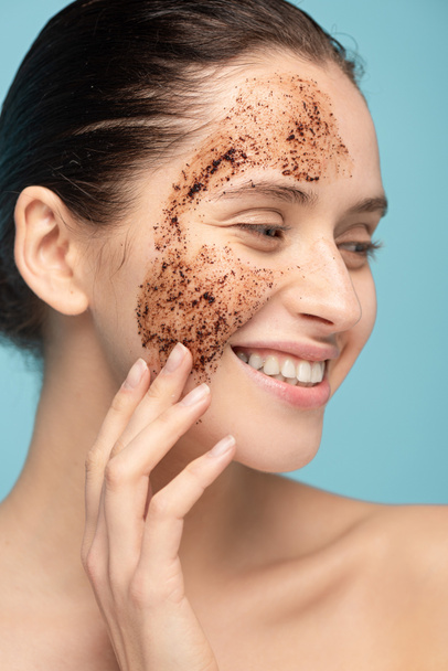 happy beautiful woman applying coffee scrub on face, isolated on blue - Photo, Image