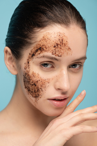 young woman applying coffee scrub on face, isolated on blue - 写真・画像