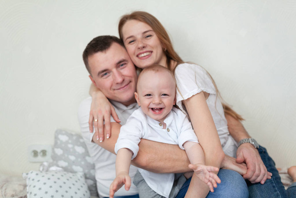 Porträt einer glücklichen jungen Familie. Eltern und Baby kuscheln und spielen auf dem Sofa im Zimmer - Foto, Bild