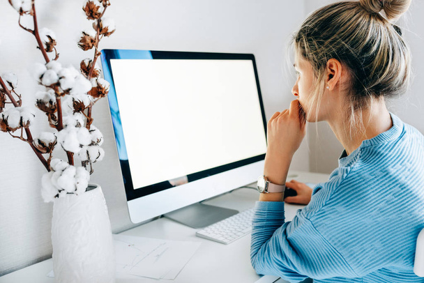 Side view of freelacer businesswoman using desktop computer in creative office. Photo of young blonde woman sit indoors at home working on computer with blank screen for your text message or content - Foto, afbeelding
