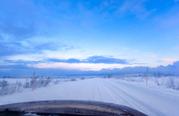 Snow Road with tire tracks above the Arctic Circle from inside the car (hood - bonnet visible at the bottom) under pale blue sky - Fotoğraf, Görsel