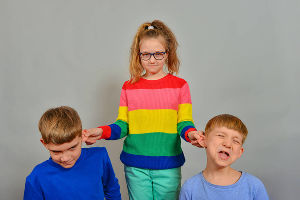 Dívka hubuje a vzdělává chlapce, a trestá své mladší bratry tím, že jim drží uši. - Fotografie, Obrázek