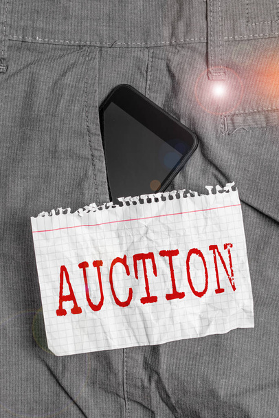 Word writing text Auction. Business concept for Public sale Goods or Property sold to highest bidder Purchase Smartphone device inside formal work trousers front pocket near note paper. - Photo, Image