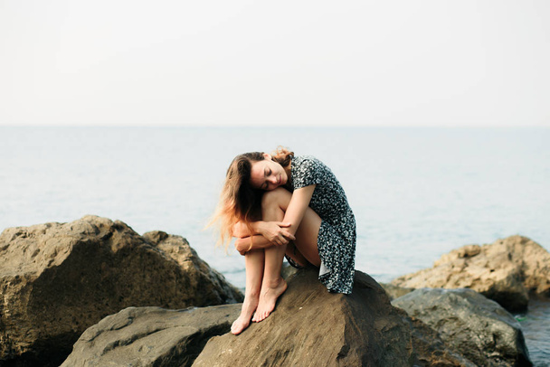 una joven hermosa niña en un vestido sobre piedras grandes, un lugar pintoresco en la costa del mar
 - Foto, imagen