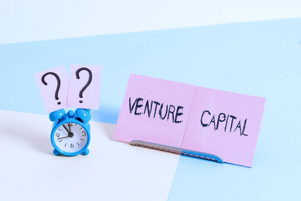 Szóírás szöveg Venture Capital. Üzleti koncepció olyan projektbe fektetett tőkére, amelyben fennáll a kockázat Mini méretű ébresztőóra a pasztell hátterére dőlt papírlap mellett. - Fotó, kép