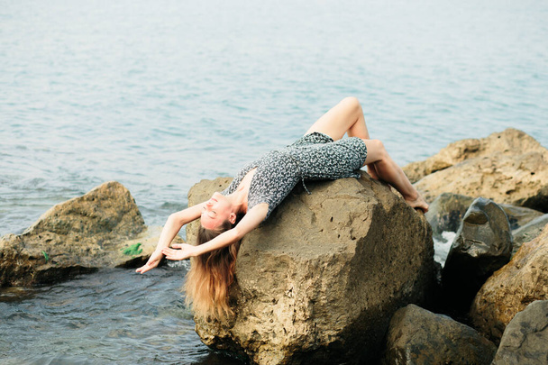 mladá krásná dívka v šatech na velkých kamenech, malebné místo na mořském pobřeží - Fotografie, Obrázek