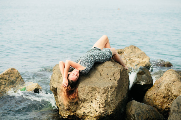 mladá krásná dívka v šatech na velkých kamenech, malebné místo na mořském pobřeží - Fotografie, Obrázek