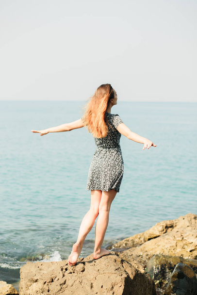una giovane bella ragazza in un vestito su grandi pietre, un posto pittoresco sulla costa del mare
 - Foto, immagini