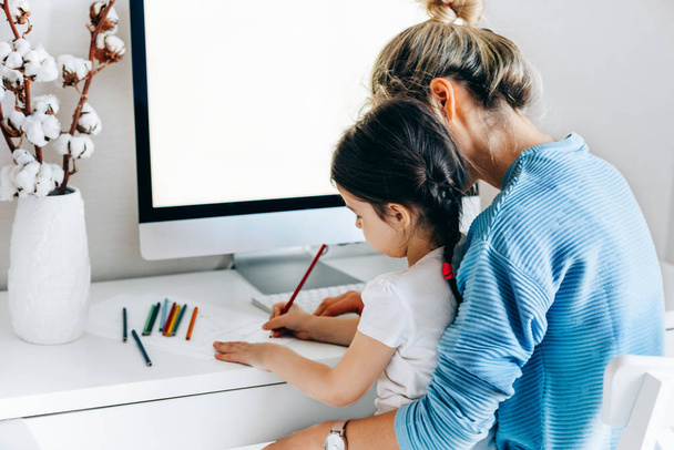 Rear view image of young woman with daughter sitting at home and working. Young mother with toddler child working at the computer and playing. Housewife mother sitting with her child and working. - Foto, Imagen