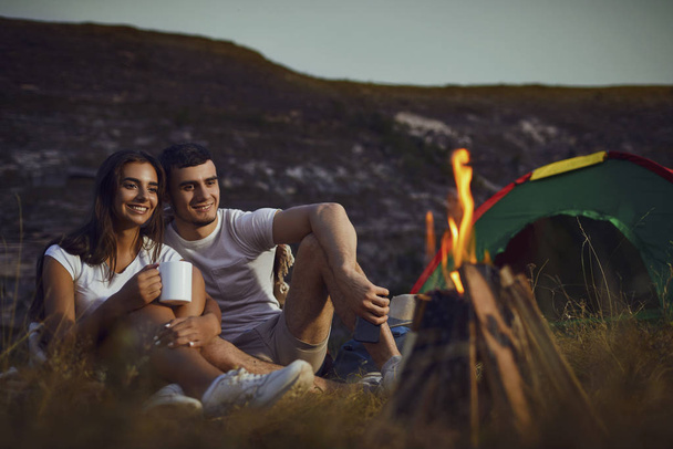 Romantic camping. A young couple sitting by the bonfire - Fotografie, Obrázek