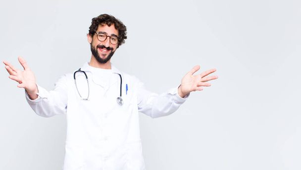 young doctor man smiling cheerfully giving a warm, friendly, loving welcome hug, feeling happy and adorable against copy space wall - Φωτογραφία, εικόνα