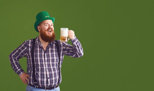 Happy St. Patricks Day. Fat man in a green hat holds his hands up glasses with beer - 写真・画像
