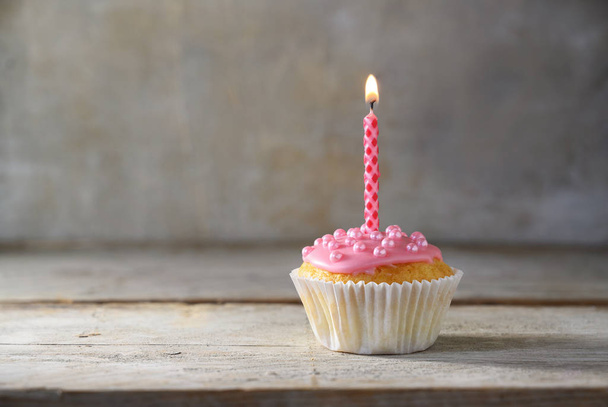 muffin nebo cupcake s růžovou hořící svíčkou na dřevěné desce na rustikálním pozadí, narozeninový koncept s kopírovacím prostorem - Fotografie, Obrázek