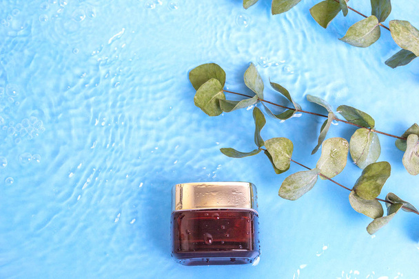Prázdná smetana sklenice proti stárnutí kolagenu obličeje s eukalyptovými listy na modré vodní hladině bazénu, horní pohled. Koncept letní kosmetiky. Přírodní organický kosmetický produkt - Fotografie, Obrázek