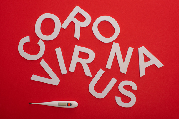 Vue du dessus du lettrage du coronavirus et du thermomètre électronique sur fond rouge
 - Photo, image