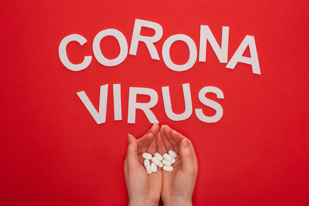 Top view of woman holding pills near coronavirus lettering on red background - 写真・画像