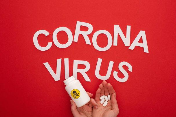 Top view of woman holding pills and jar with warning sign near coronavirus lettering on red background - Photo, image