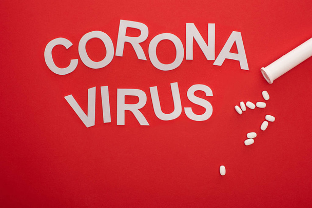 Top view of coronavirus lettering and pills on red background - Foto, Imagen