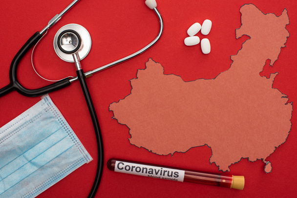 Vista superior del estetoscopio, máscara médica y tubo de ensayo con letras de coronavirus cerca del mapa de China sobre fondo rojo
 - Foto, imagen
