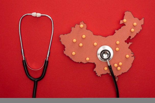 Vue du dessus de la carte de la Chine avec broches poussoirs et stéthoscope sur fond rouge
  - Photo, image
